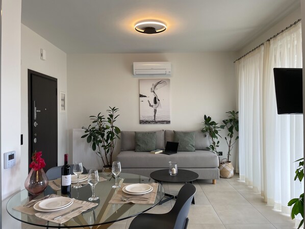Uma sala de estar moderna com mesa de jantar de vidro, sofá cinza e um quadro na parede.