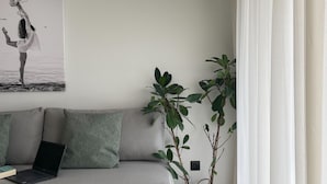 A modern living room with a grey sofa, a laptop, a potted plant, and a wall-mounted air conditioner. - MOSSA CITY APARTMENTS (Chania)