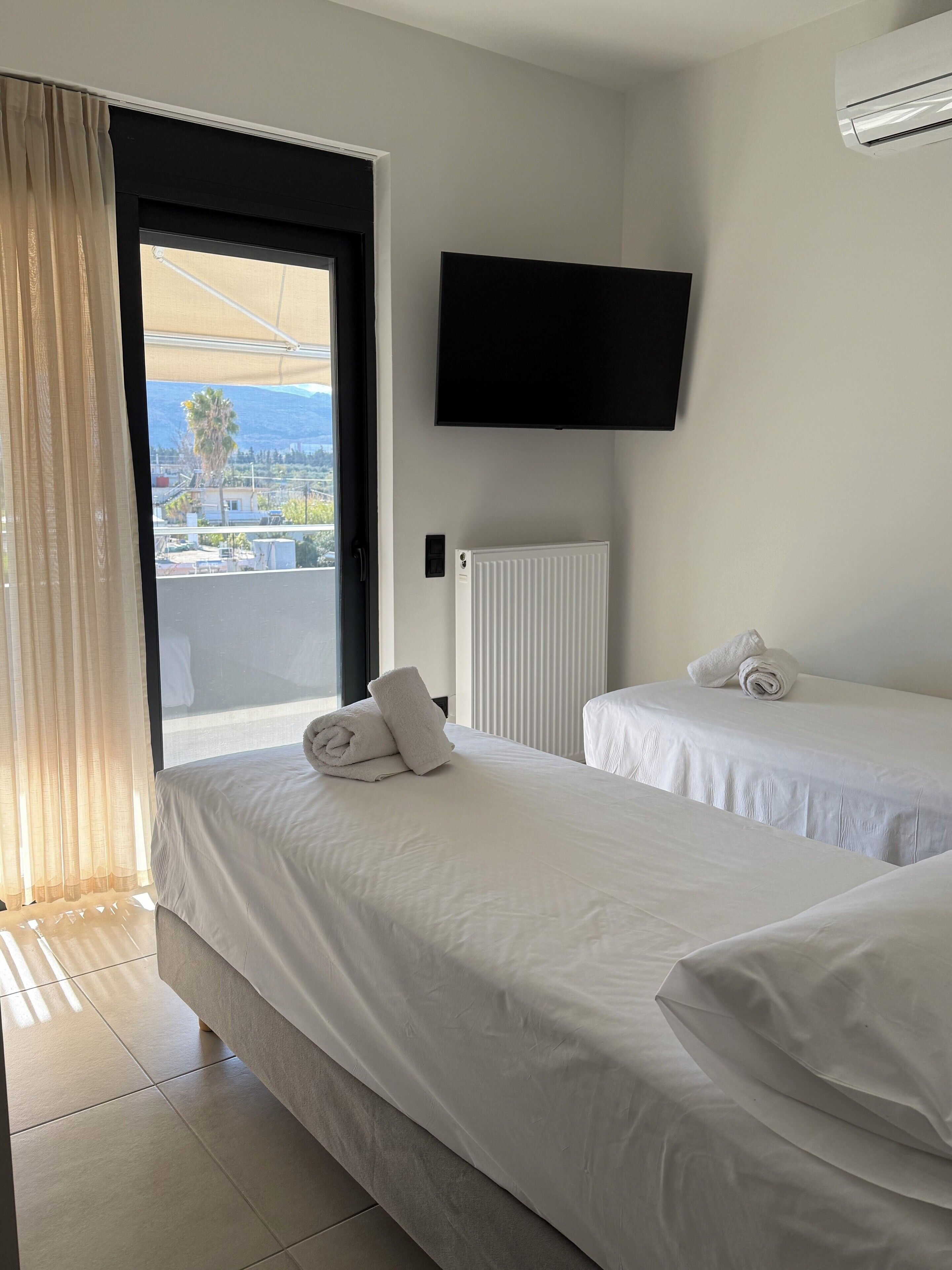 A hotel room with two beds, a TV mounted on the wall, and a view of the outdoors through a large window.