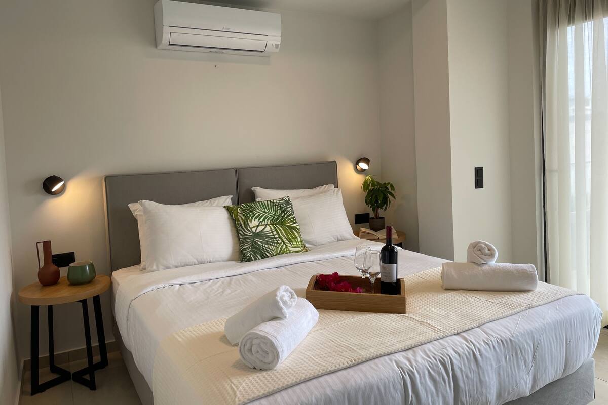 Ein Hotelzimmer mit Bett, Nachttischen, einer Klimaanlage, einer Topfpflanze und einem Fenster mit Vorhängen.