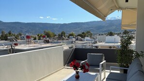 A balcony with a white table, two grey sofas, and a vase with red flowers. - MOSSA CITY APARTMENTS (Chania)
