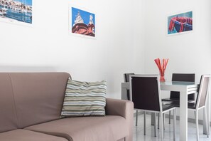 A modern living room with a sofa, a dining table with chairs, and artwork on the walls.