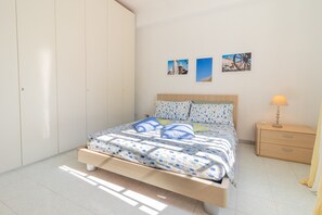 A bedroom with a bed, a nightstand, a lamp, and wall-mounted pictures.