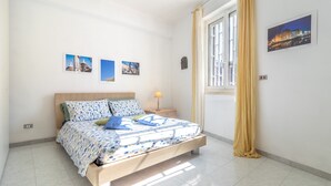 A bedroom with a bed, a nightstand, a lamp, a window with curtains, and wall art. - Esperia Home penthouse in Bari with private terrace, Wi-Fi, and air conditioning (Bari)