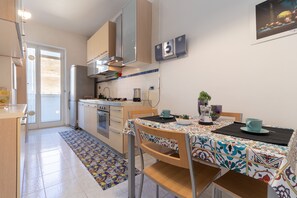 A modern kitchen with a dining area, featuring a patterned tablecloth, wooden chairs, and a coffee machine.