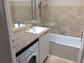 Ein Badezimmer mit Granitwaschtisch, Waschbecken, Waschmaschine und Badewanne.