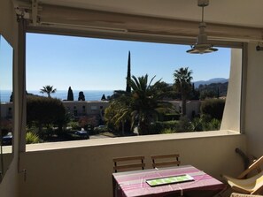 Ein Balkon mit Tisch und Stühlen, der auf einen Wohnbereich mit Palmen und freiem Blick aufs Meer blickt.