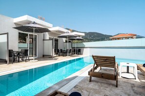 A pool area with a wooden bench, outdoor seating, and umbrellas.
