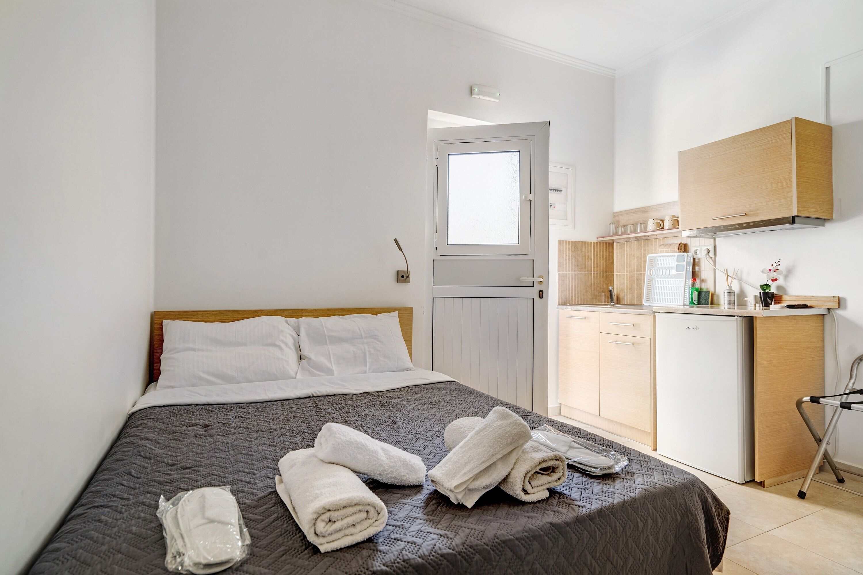 A hotel room with a bed, a small kitchenette, and a door leading to a bathroom.