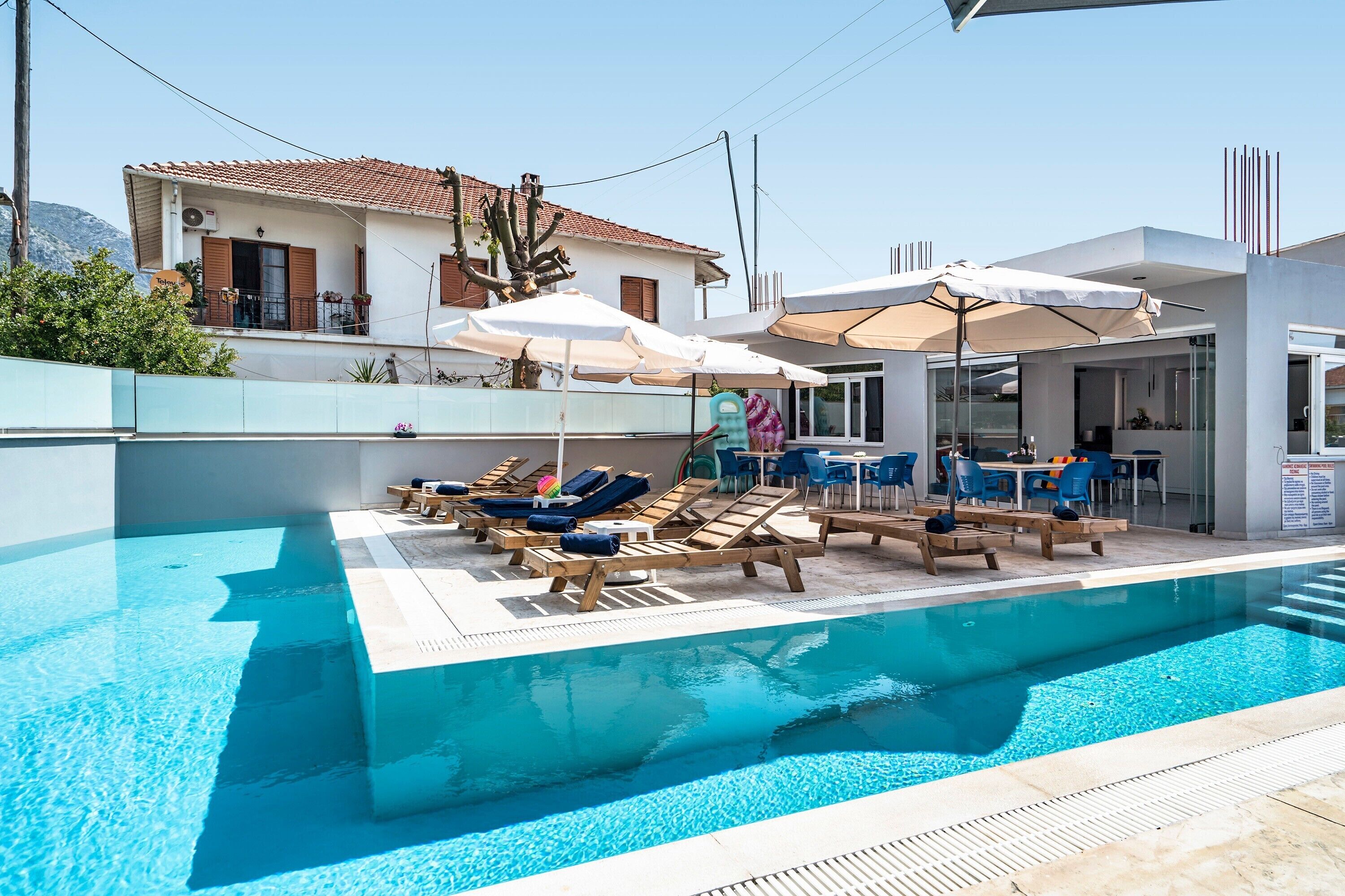 A swimming pool with lounge chairs and umbrellas, a modern building with a tiled roof, and a mountain in the background.