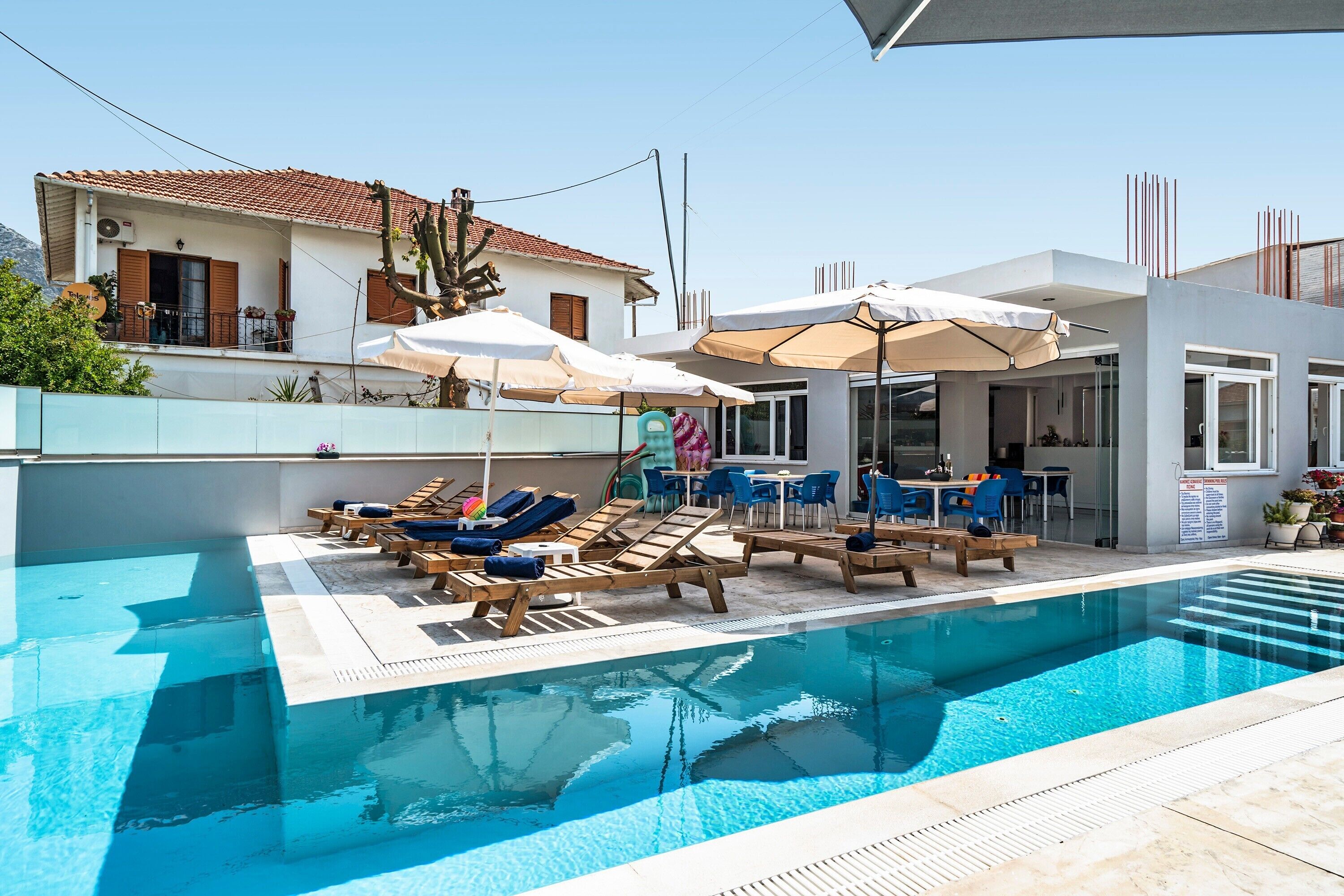 A swimming pool with lounge chairs and umbrellas, a patio area, and a building with a tiled roof.