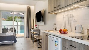 A modern kitchen with a dishwasher, a TV mounted above the counter, and a dining area with a bench and table. - Studio 'King Room with Pool View' with Shared Pool, Wi-Fi and Air Conditioning (?e???da?)