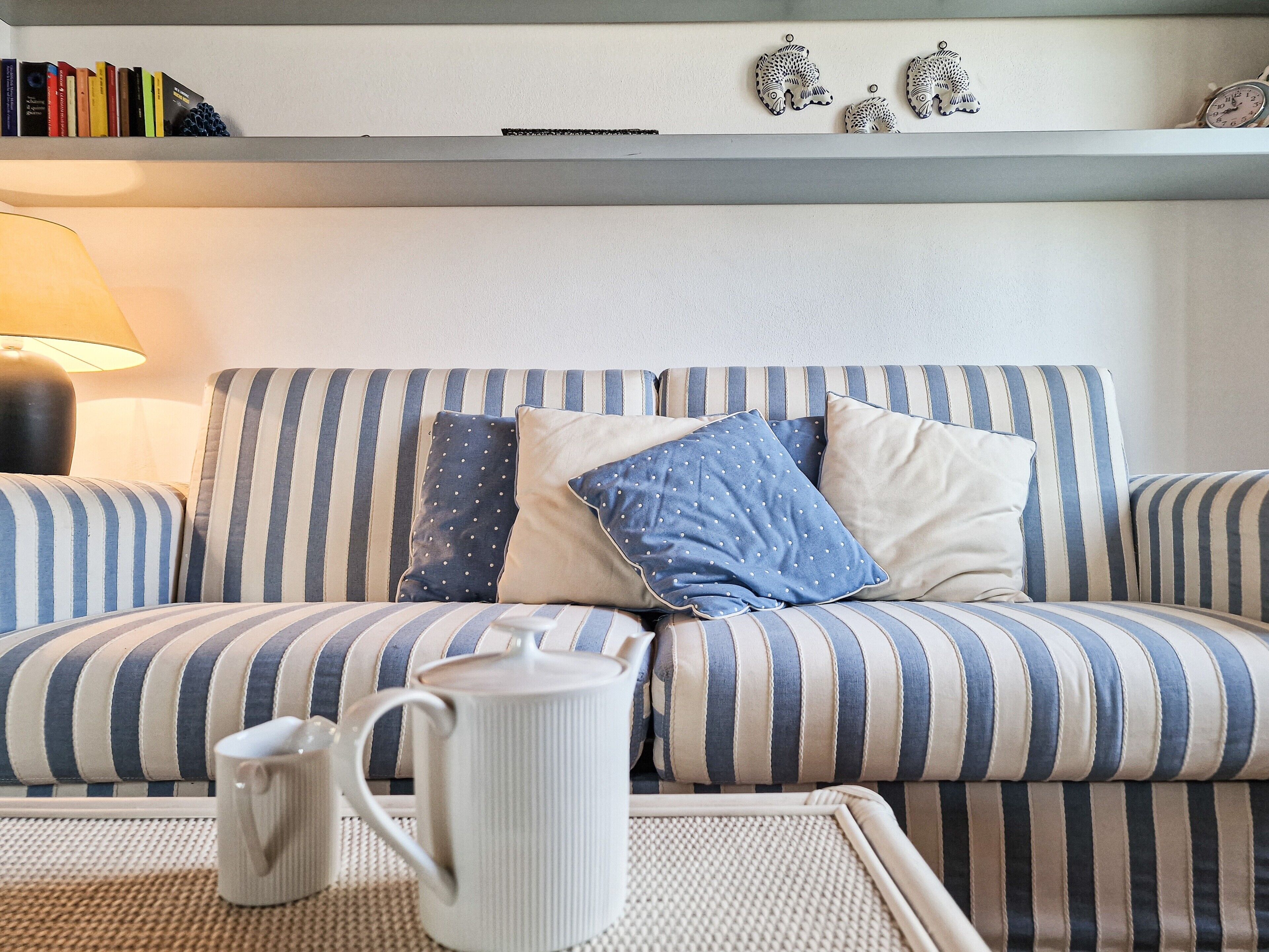 Un sofá a rayas con almohadones, una taza blanca y objetos decorativos en un estante.
