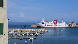 A harbor with a large ship named 'Toremar' docked, surrounded by smaller boats, and a rocky breakwater.