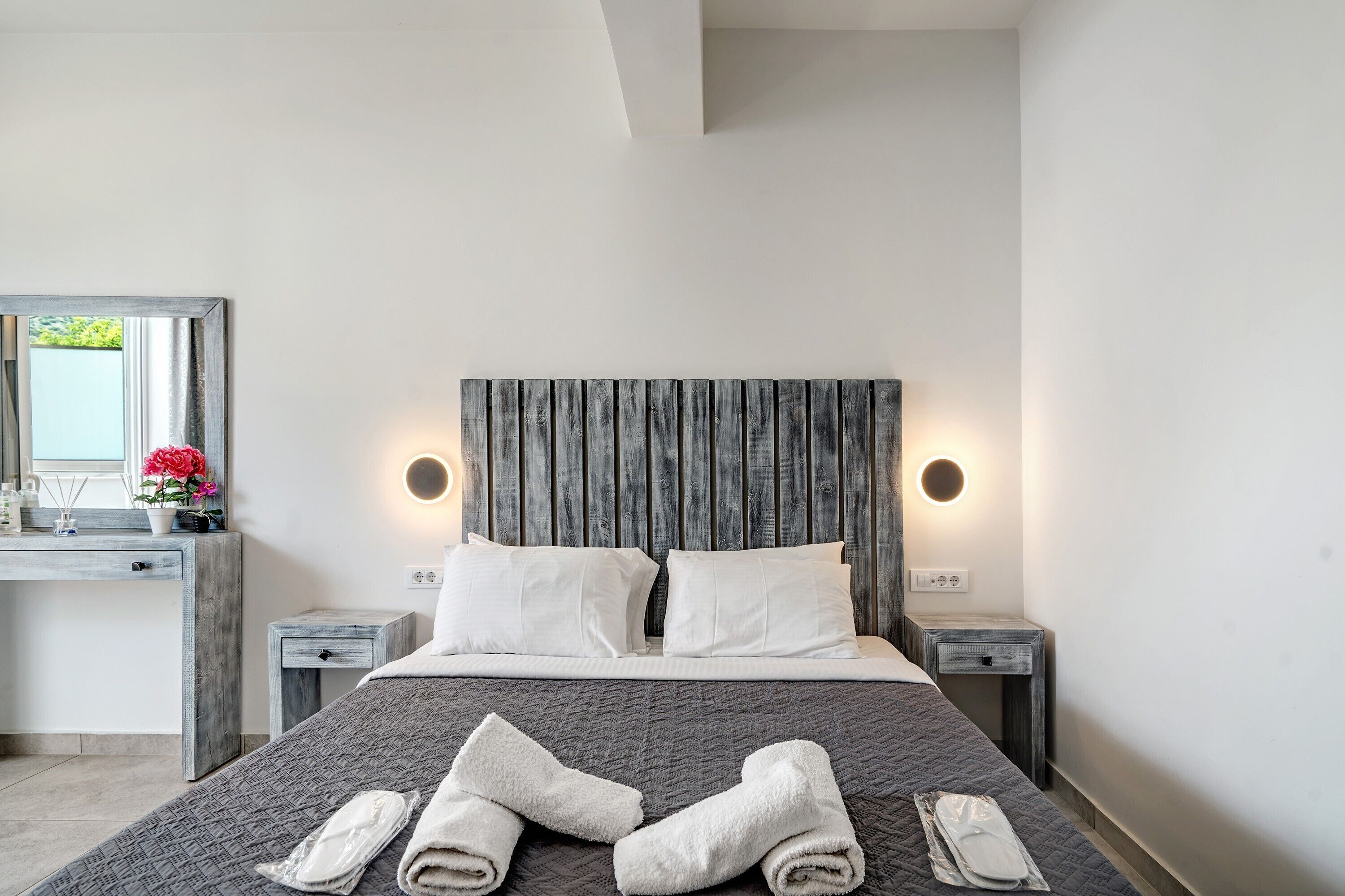 Ein Schlafzimmer mit Bett, zwei Nachttischen, einem Schminktisch, einer Kommode, einem Spiegel und einem Fenster.