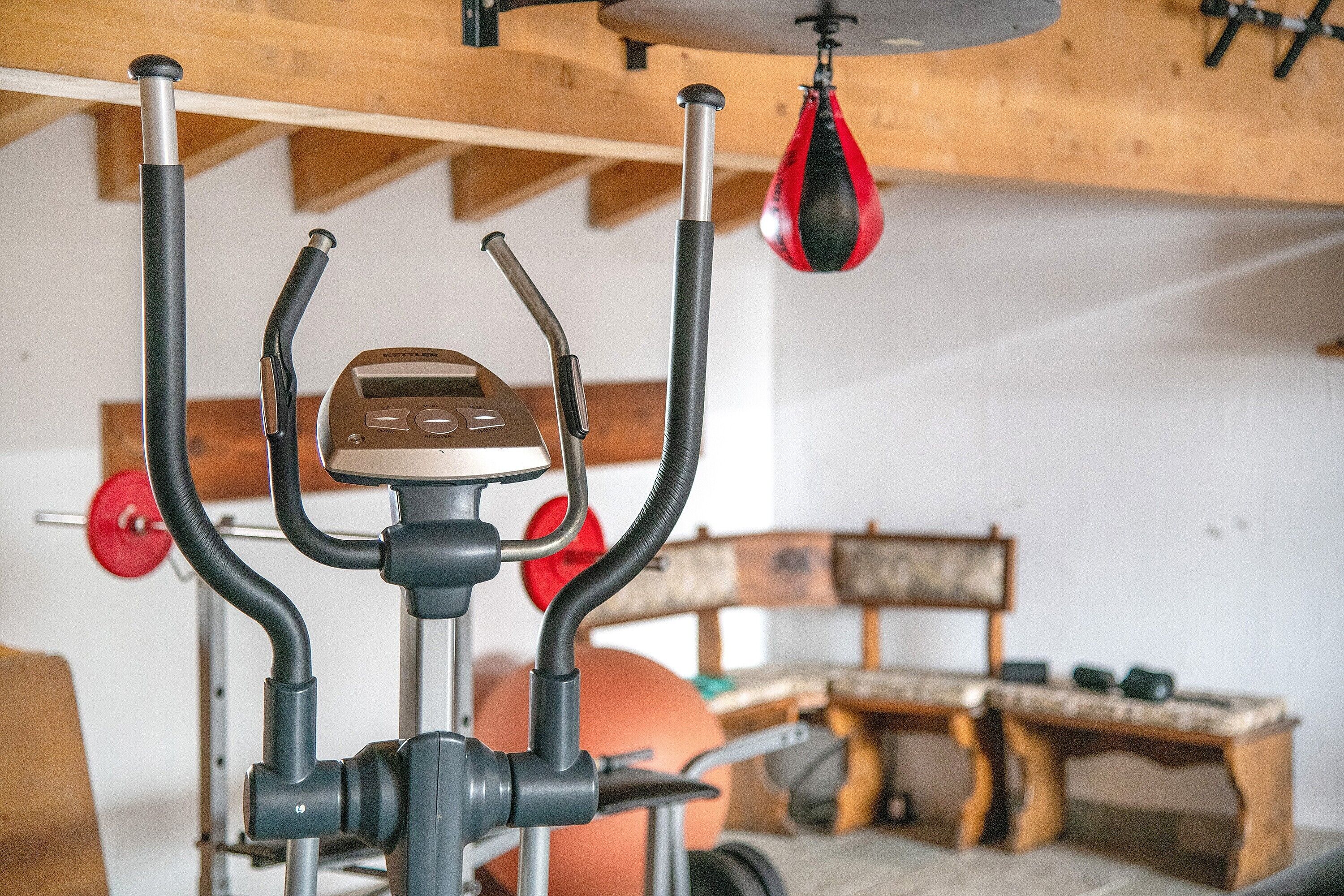 Une salle de sport équipée de matériel d’exercice, d’un sac de frappe et d’un banc en bois.