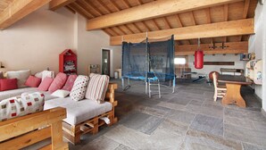 Una habitación amplia con techo de madera alto, un trampolín, una mesa de madera y un sofá con cojines.