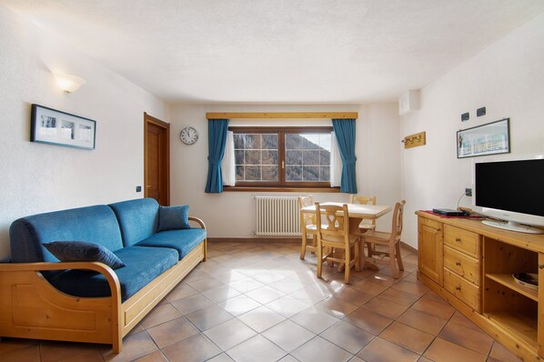 Une pièce comprenant un canapé, une table à manger avec des chaises, un téléviseur posé sur un meuble en bois et une fenêtre avec des rideaux.