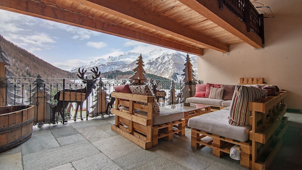 Una terraza de madera con un sofá y sillas, una mesa de madera y vistas a las montañas.
