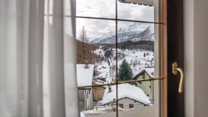 Vista desde una ventana de un paisaje nevado con montañas, casas y una pista de esquí.