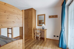 Une chambre avec un lit superposé, une armoire en bois, un bureau avec une chaise, un miroir et une fenêtre avec des rideaux.