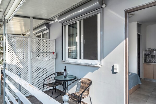 A balcony with a table and chairs, a bottle of wine, and a window.