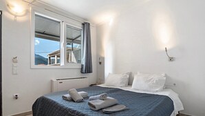 Une chambre d’hôtel avec un lit, une fenêtre avec des rideaux, une lampe fixée au mur et une vue sur un bâtiment à l’extérieur.