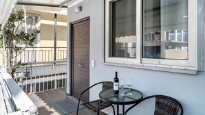 Un balcon avec une table, des chaises, une bouteille de vin et une fenêtre.