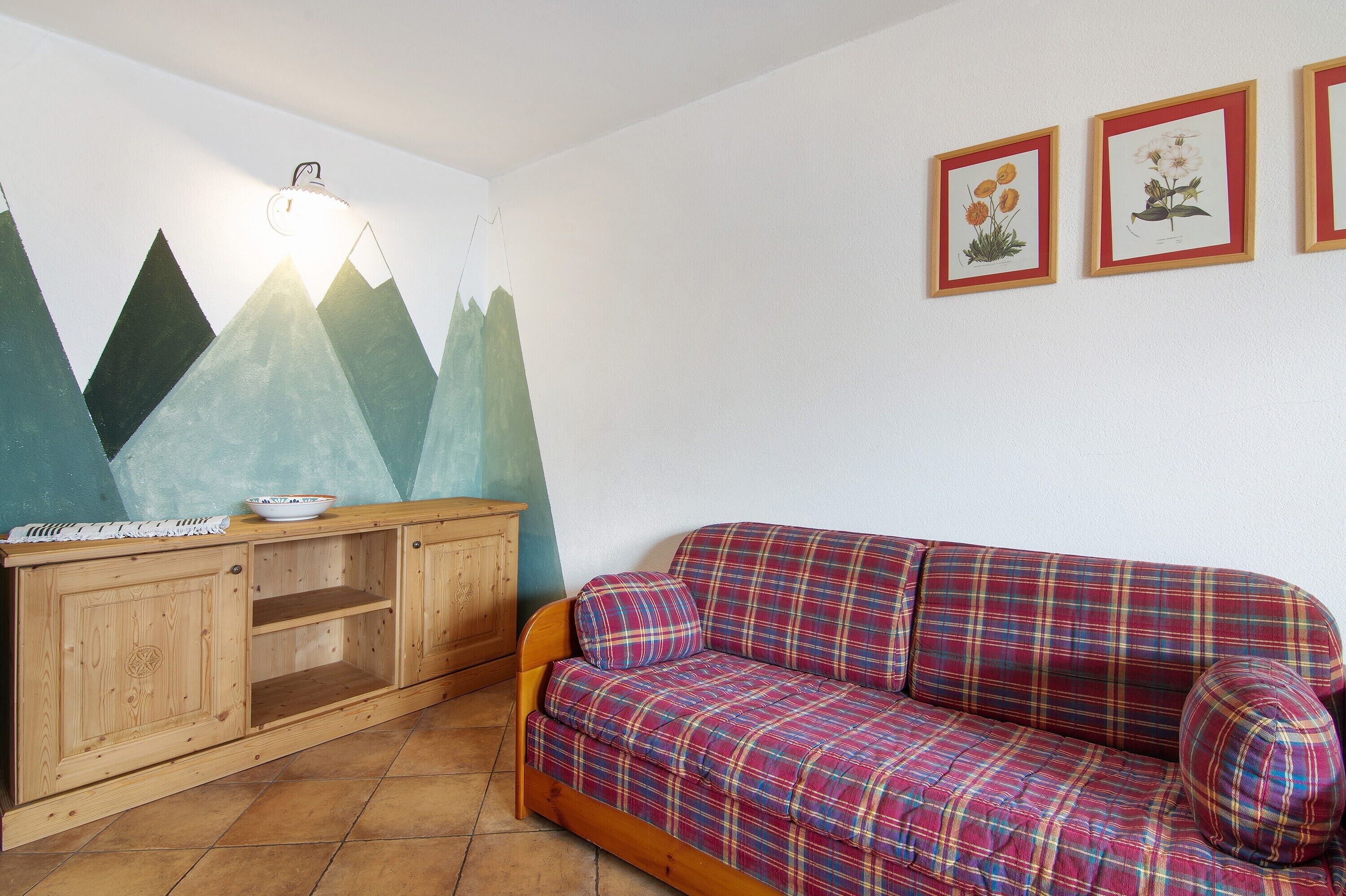 Ein Zimmer mit einem karierten Sofa, einem Holzkabinett und Wandbildern.