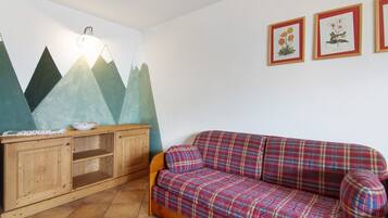 Ein Zimmer mit einem karierten Sofa, einem Holzkabinett und Wandbildern.