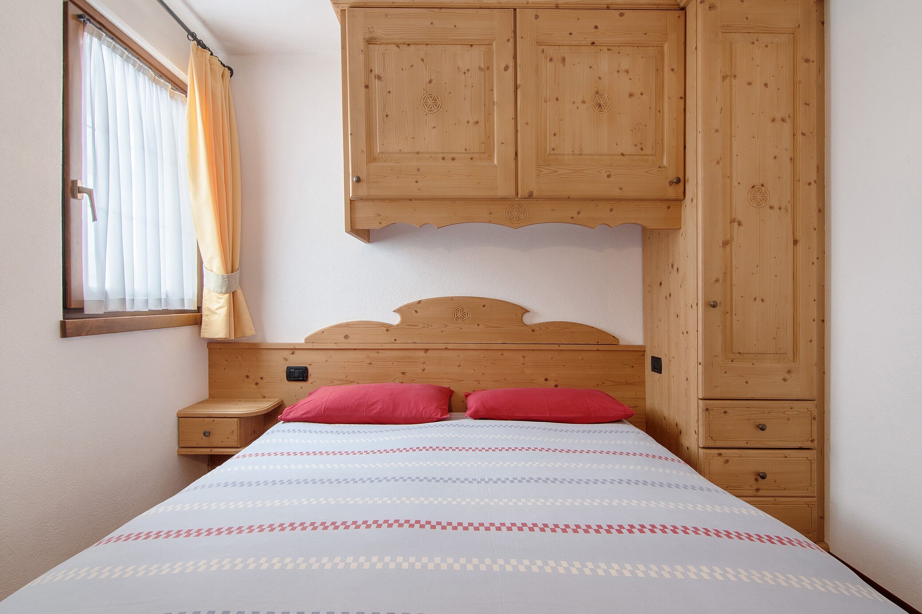 Una camera da letto con una testiera in legno, un letto con biancheria a motivi, un comodino e un armadio in legno.