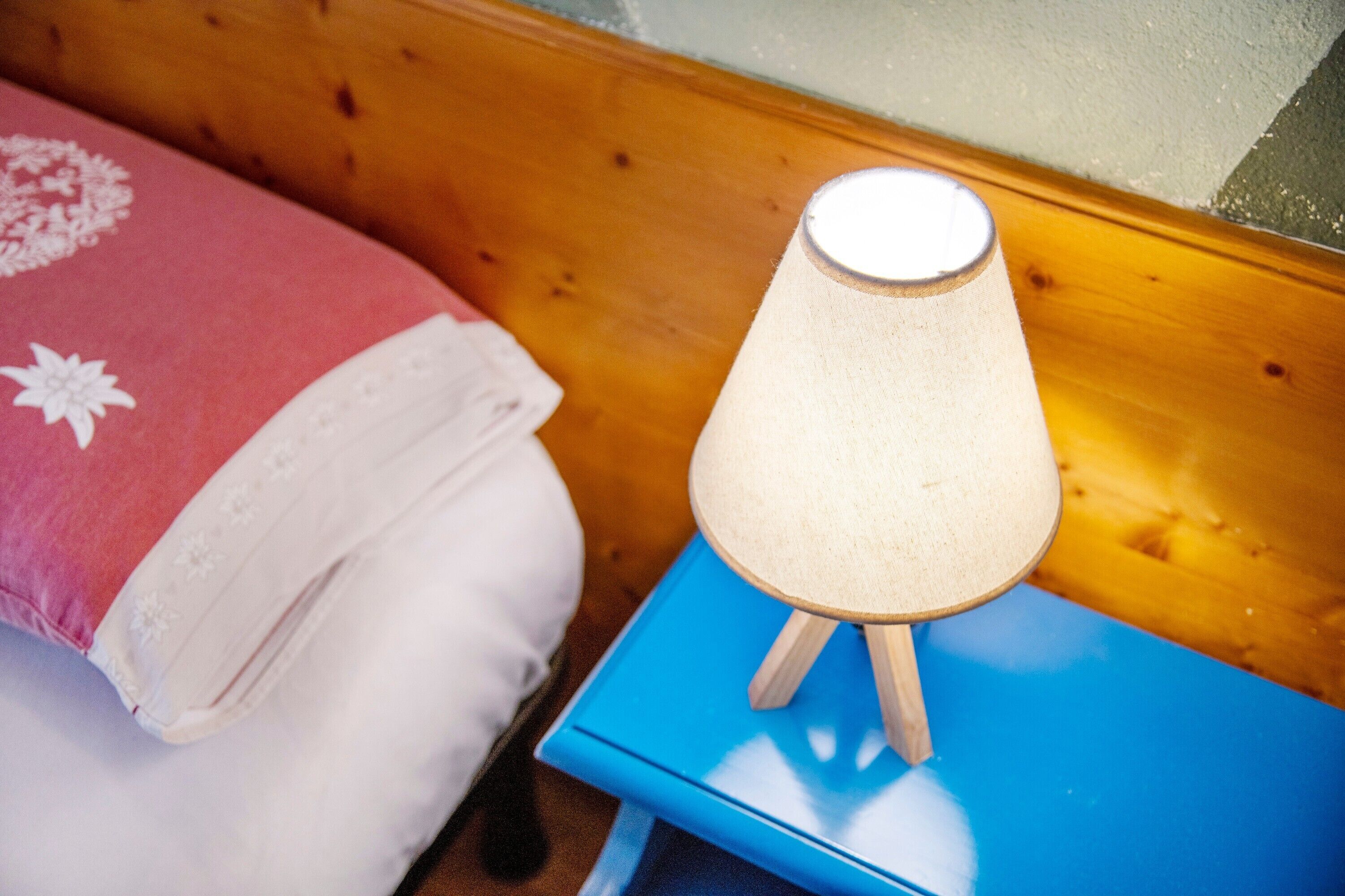 Un lit avec un oreiller rose et blanc, une table de chevet bleue avec une lampe, et une tête de lit en bois.