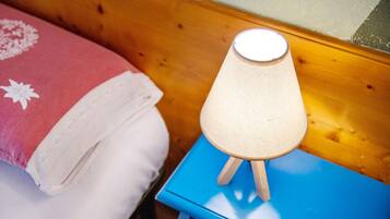 Un lit avec un oreiller rose et blanc, une table de chevet bleue avec une lampe, et une tête de lit en bois.