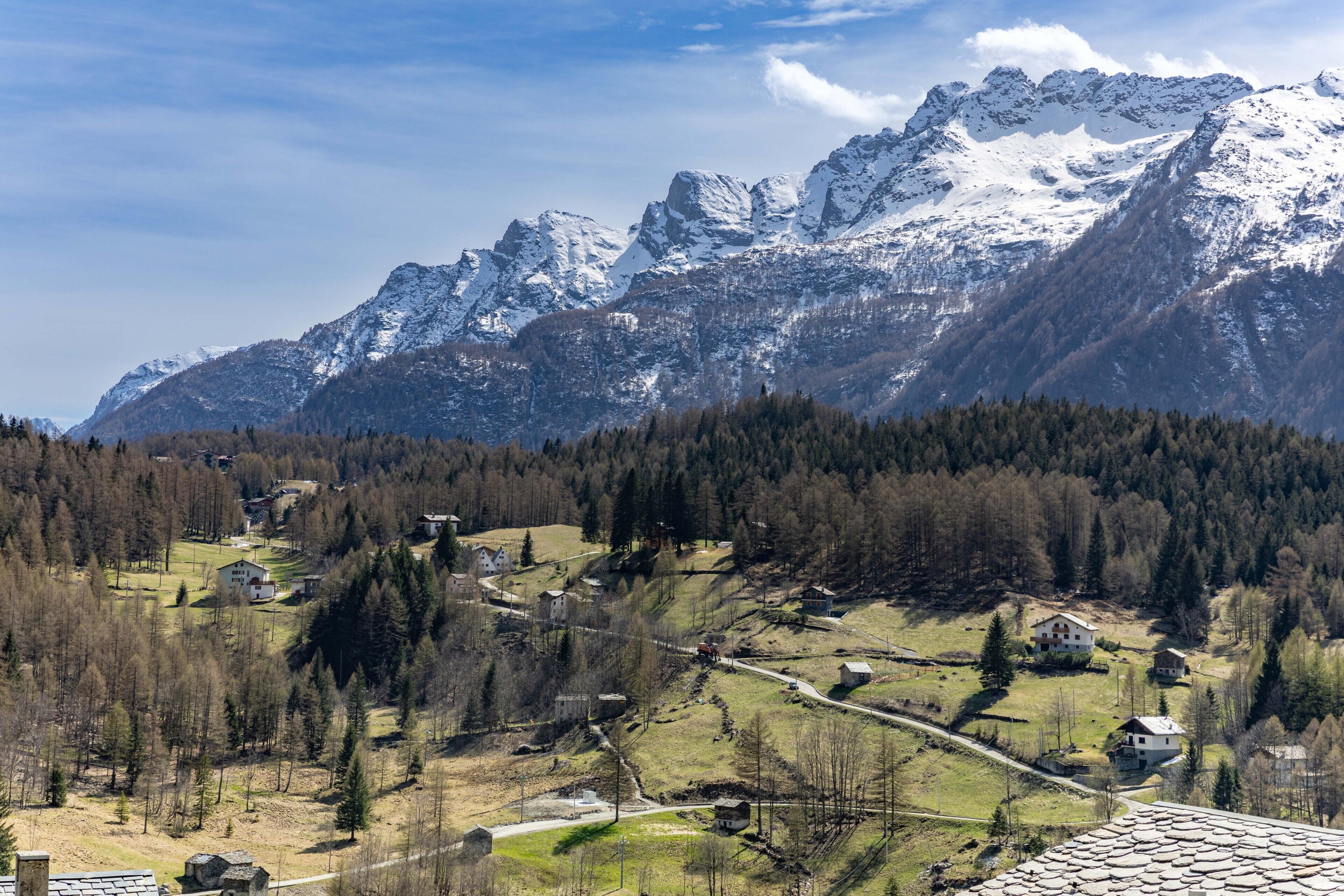 A mountainous landscape with snow-capped peaks, a valley with scattered houses, and a clear sky.