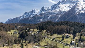 A mountainous landscape with snow-capped peaks, a valley with scattered houses, and a clear sky.