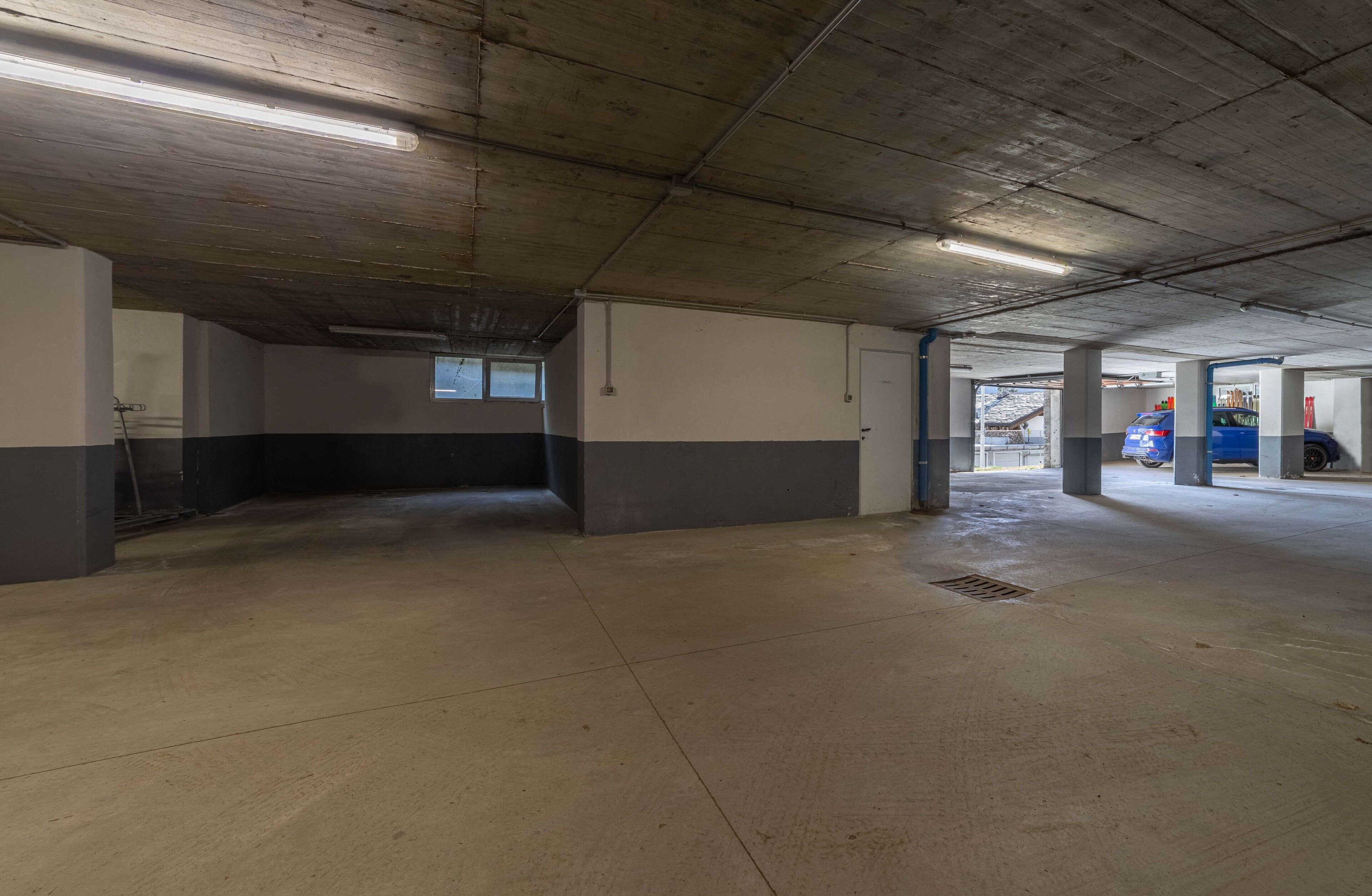 Un parcheggio coperto con pavimenti e pareti in cemento, illuminazione al neon e alcune auto parcheggiate.