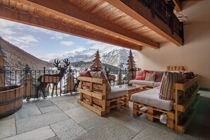 Une terrasse en bois avec un canapé et des fauteuils, une table en bois et une vue sur les montagnes.