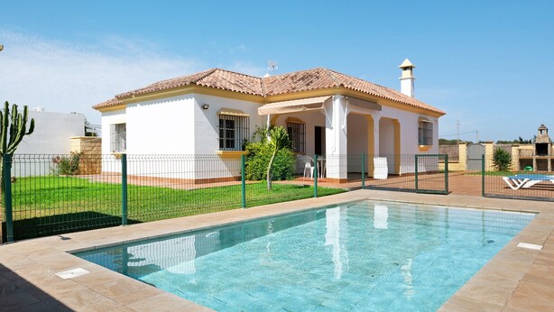 Uma casa com piscina, quintal cercado e céu claro.