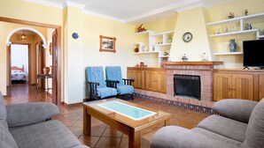 Uma sala de estar com lareira, duas poltronas azuis, uma mesa de centro e uma televisão.