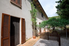 Un patio con un edificio, contraventanas de madera, un árbol en maceta y una valla de madera.