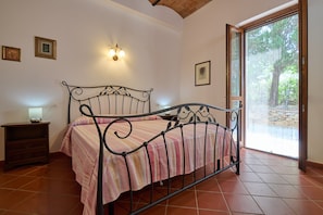 Un dormitorio con cama, mesita de noche, luz empotrada en la pared y ventana con vista a árboles.