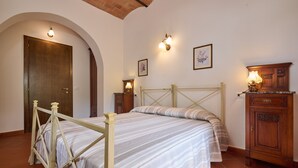 Ein Schlafzimmer mit einem Bett, einem Holzkopfende, zwei Nachttischen mit Lampen, einem Schrank und einer Tür mit rundbogigem Durchgang.