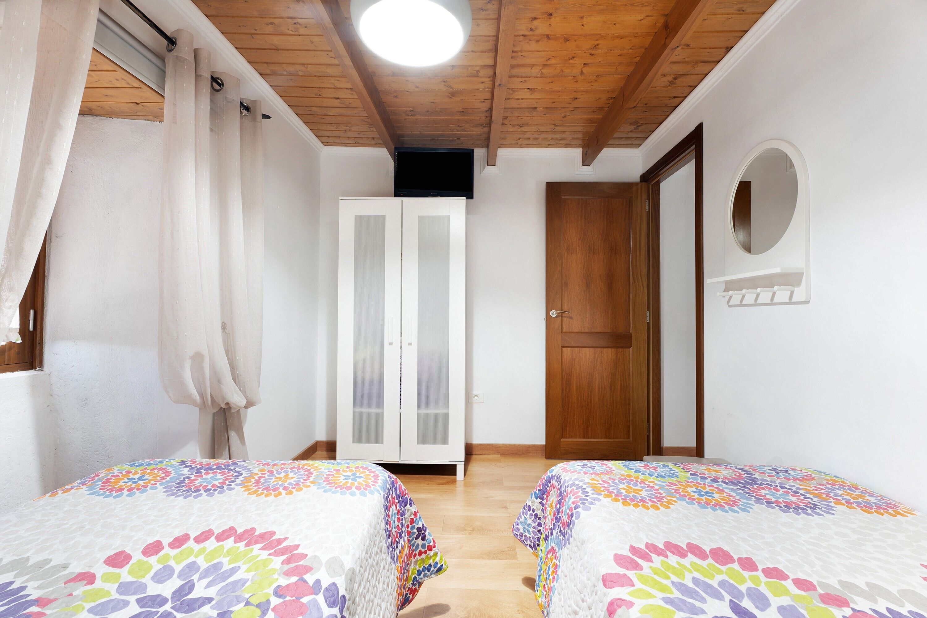 A bedroom with two beds, a wardrobe, a television, and a wooden ceiling.