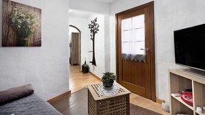 A living room with a sofa, a television, a wooden door, and a hallway leading to another room. - Rural Holiday Home 'Alto Prado' with Sea View, Private Terrace and Wi-Fi (Valverde)