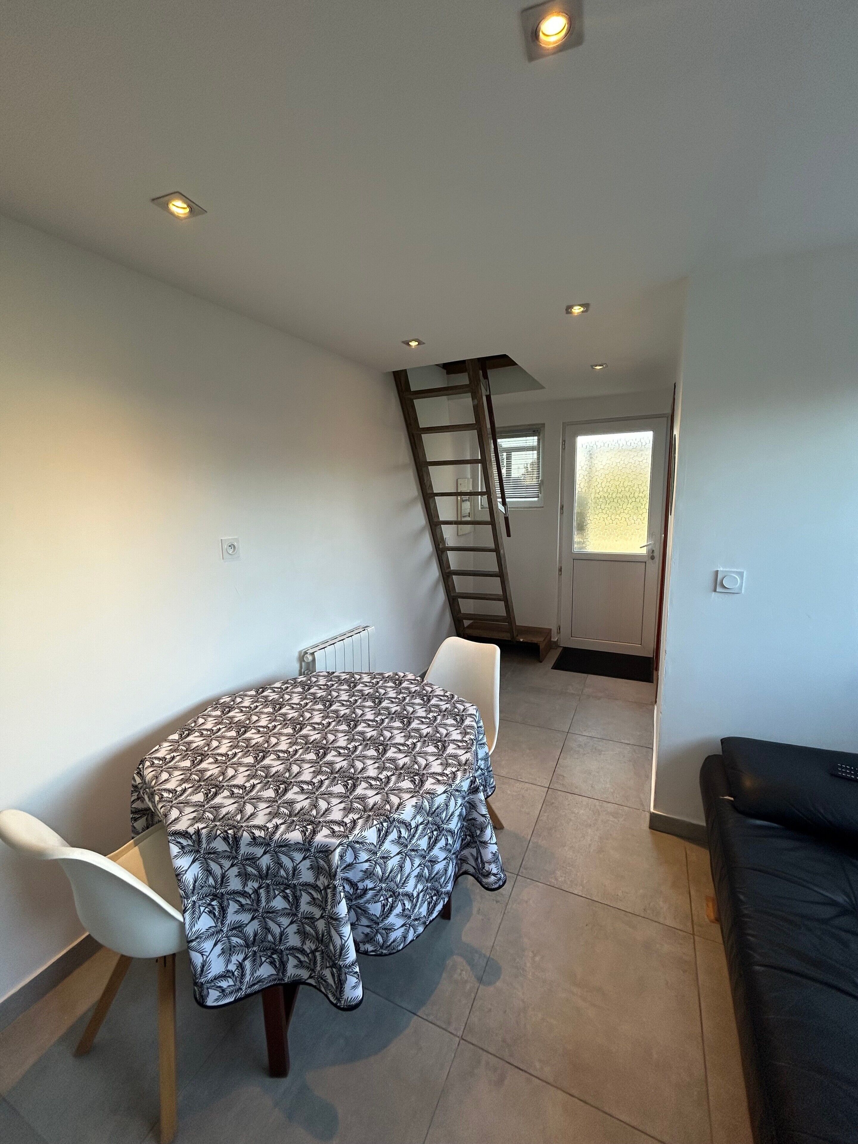 Un comedor con una mesa redonda, sillas, una escalera y una puerta que da a otra habitación.