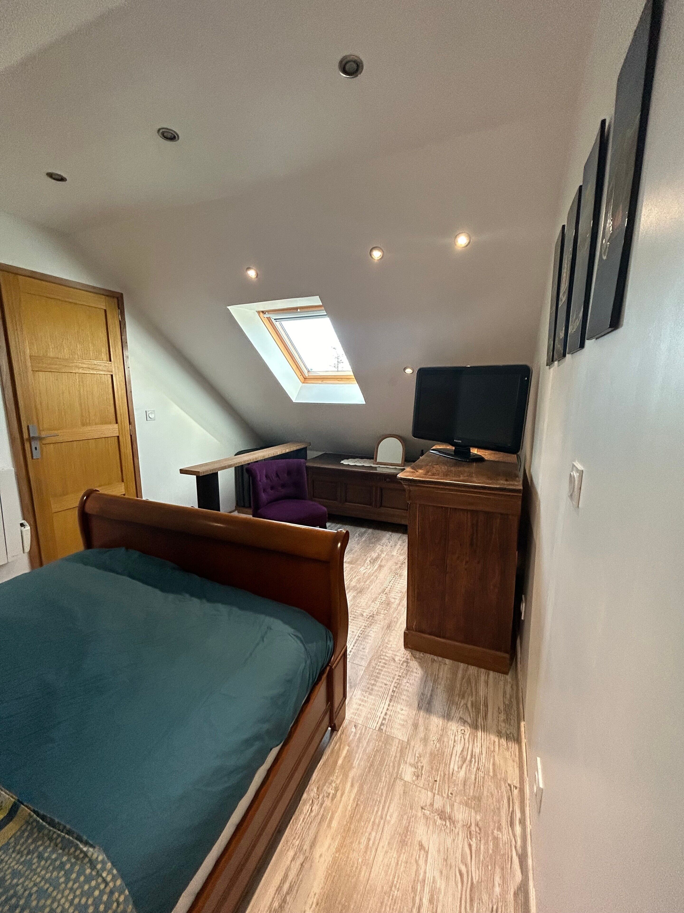 Een compacte kamer met een bed, een bureau, een stoel, een televisie en een dakraam.