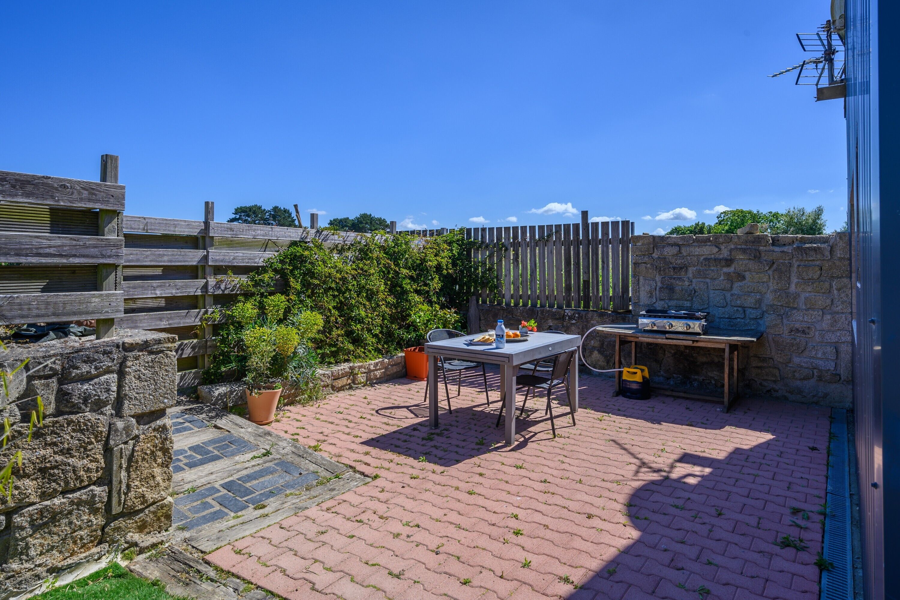 A patio with a table and chairs, a barbecue grill, and a stone wall.