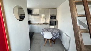 A narrow hallway leading to a kitchen with white cabinets, a microwave, and a table with a patterned tablecloth. - Petit duplex proche mer (Plouhinec)