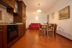 A kitchen with wooden cabinets, a red sofa, a dining table with chairs, and a painting on the wall. - Farmhouse "Antichi Palmenti - Alloro" with Shared Garden & A/C (San Vincenzo)