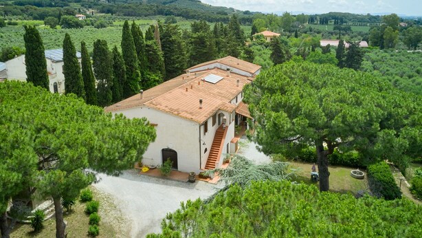 Eine Villa mit Ziegeldach, umgeben von Bäumen und Hügeln.